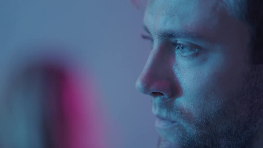 A man looking despondent turns his head and watches people walk by
