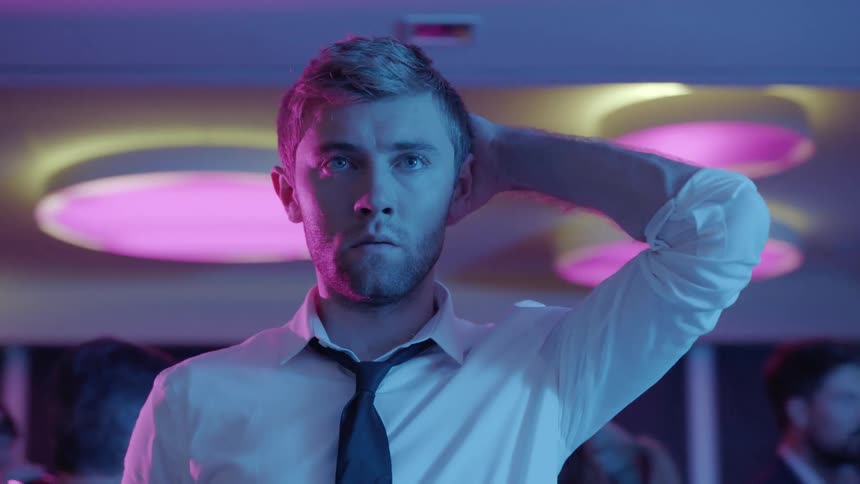 Man stands alone staring at the club under colored lighting