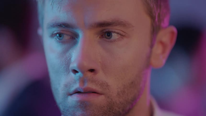 A man is in a room looking around and there are other people moving behind him