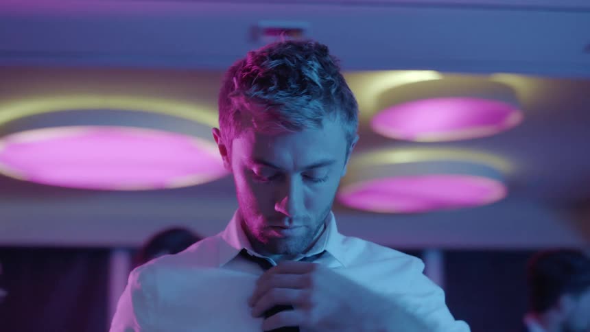 A man runs his hand over his hair and adjusts his necktie at a party