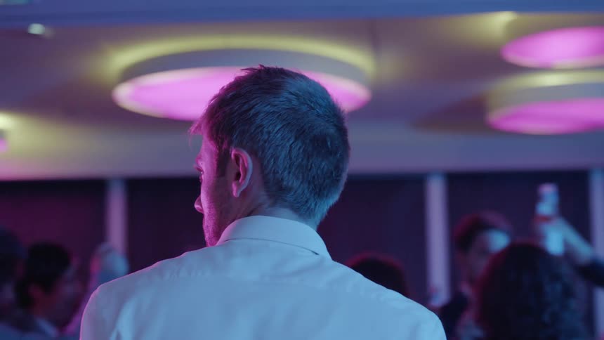 A man stands alone amidst a crowd of people at a party while looking nervous