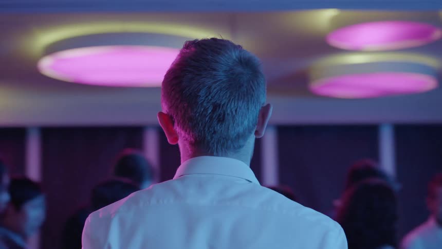 People are dancing at a party as a man watches from the side