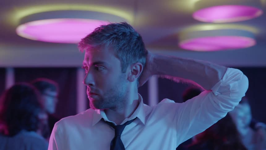 Man stands alone at party under colored lights and looks around