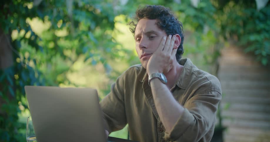 A man works on his laptop while sitting outside on a patio