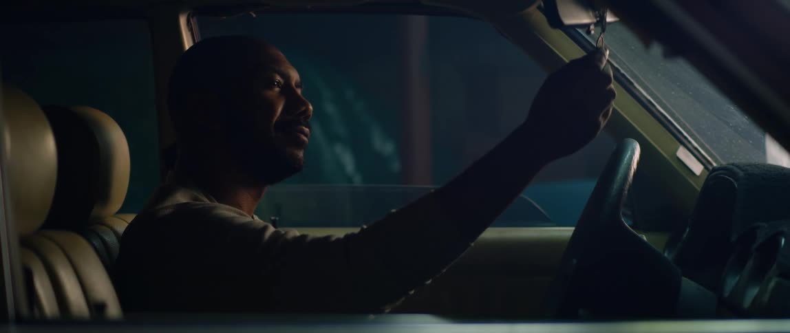 A man sitting in his parked car holds and caresses a medal hanging from the rearview mirror