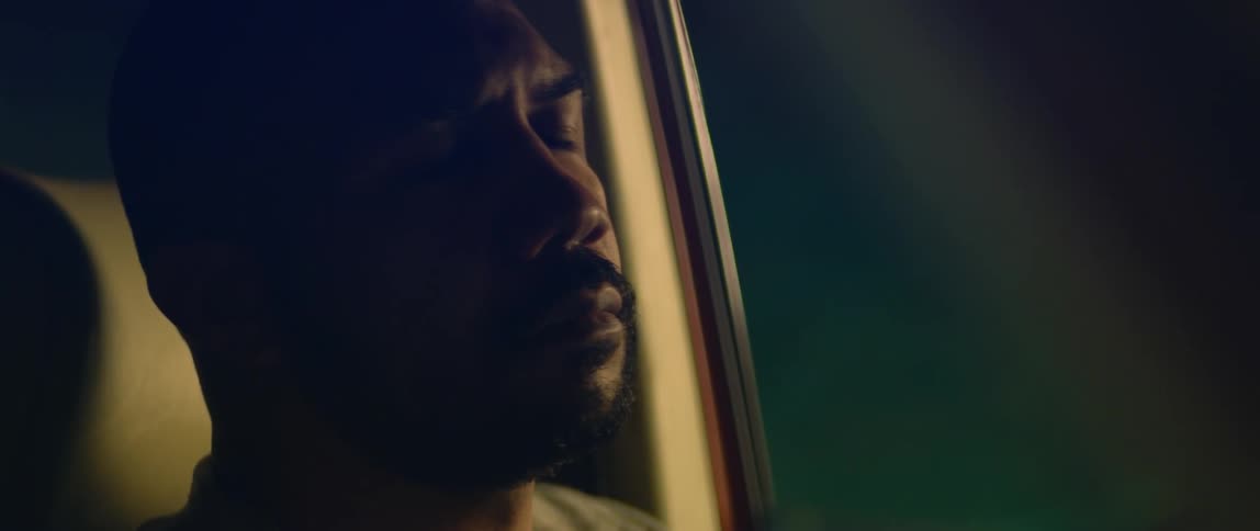 Bald bearded man sitting on the driver seat of a car parked inside a dimly lit garage