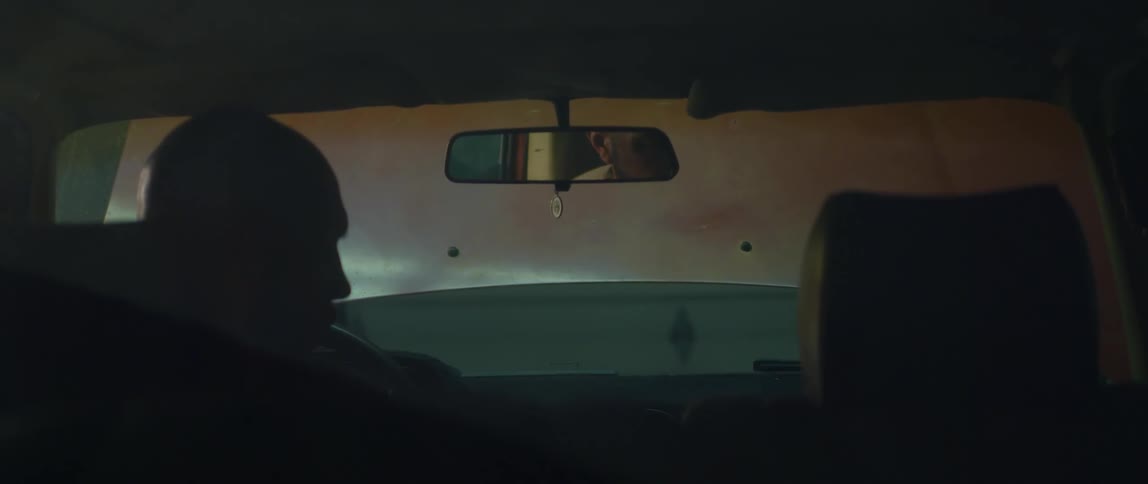 A man is sitting in the drivers seat of an automobile and he looks out the window