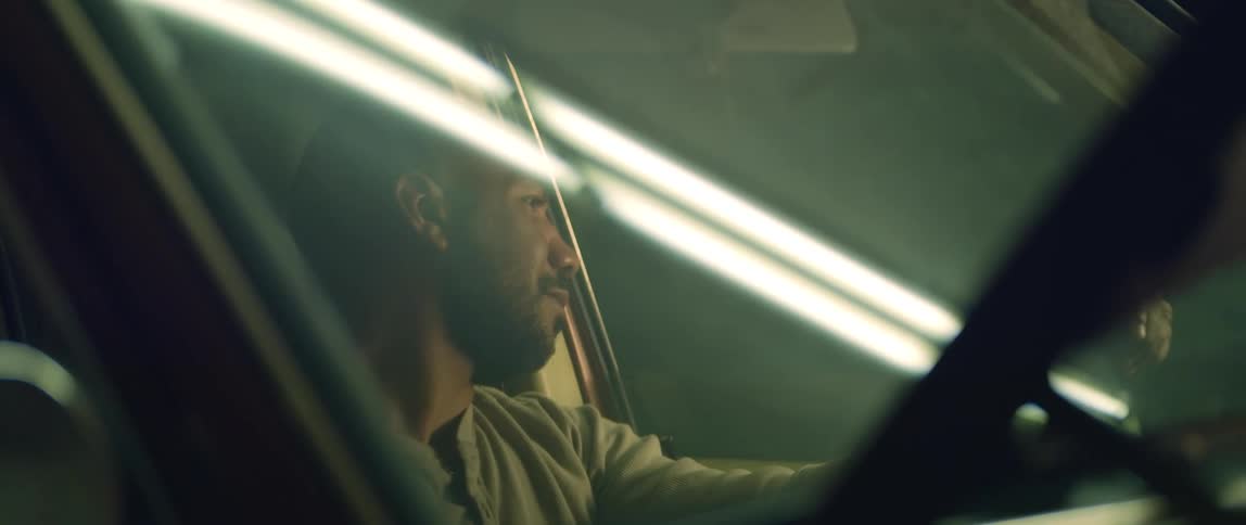 A man sits in his car with the hood up and looks out the window