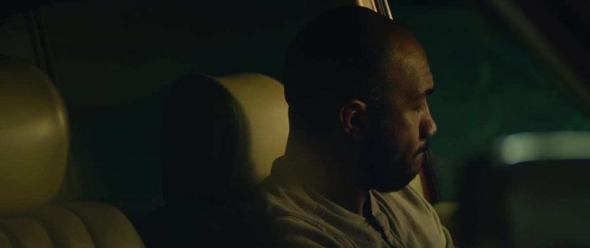 Bald bearded man sitting on the driver seat of a car parked inside a dimly lit garage