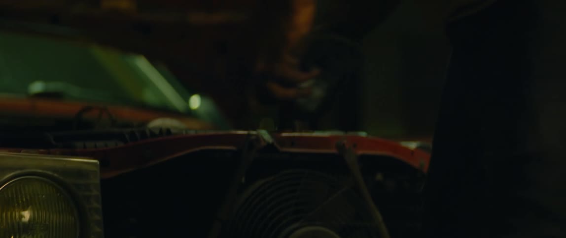 Crouching man stands and turns to look at engine of nearby car