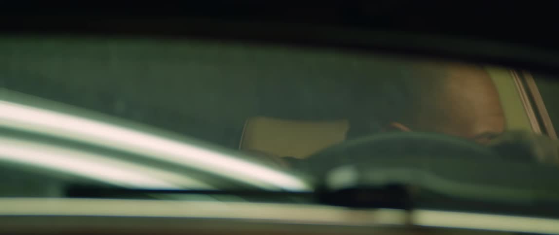 A man is sitting in the drivers seat of a parked automobile and he opens the door and gets out