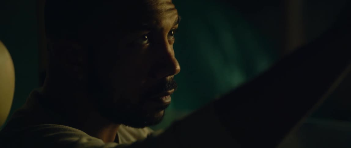 A man sits in his car at night and looks in the rear view mirror