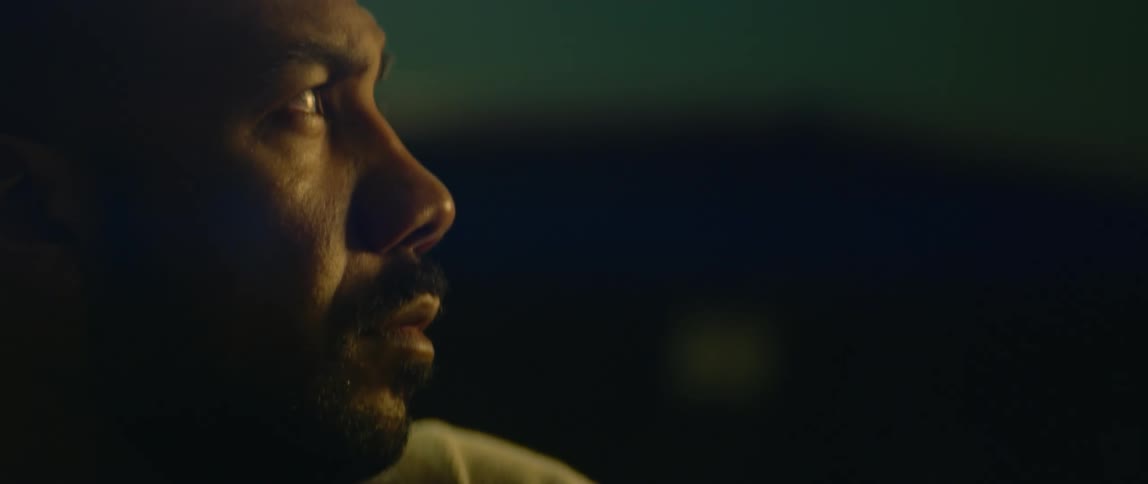 Close up of the face of a bald bearded man working inside a dimly lit garage