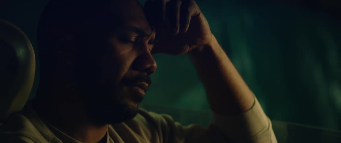 A man is sitting in the drivers seat of a parked automobile with his eyes closed and he leans his head on his hand