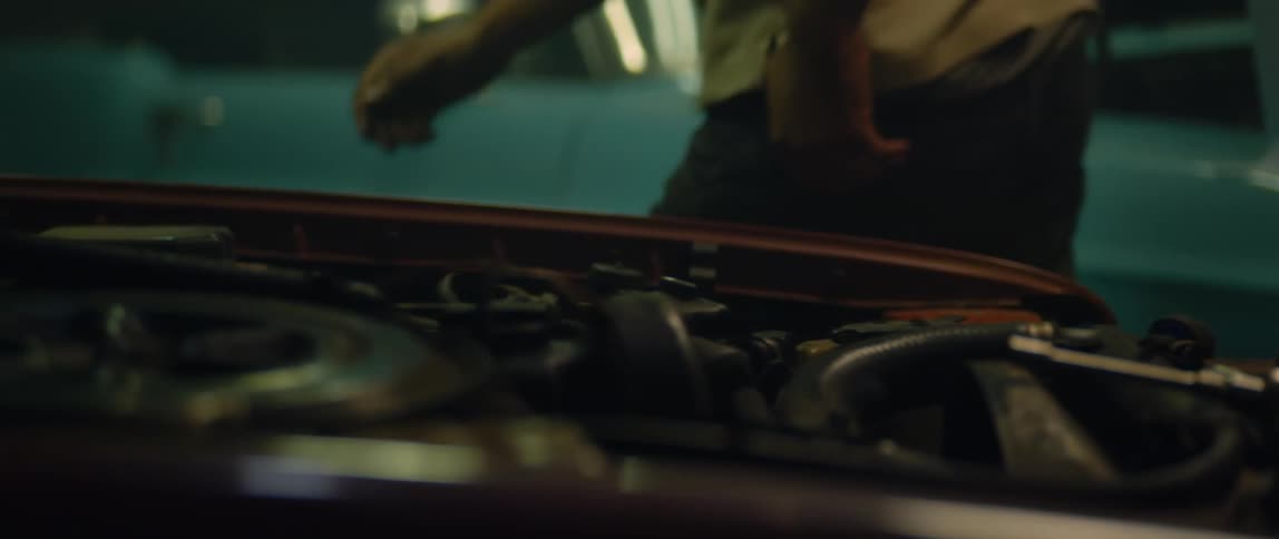 Mechanic walks around a vehicle parked inside a dimly lit garage