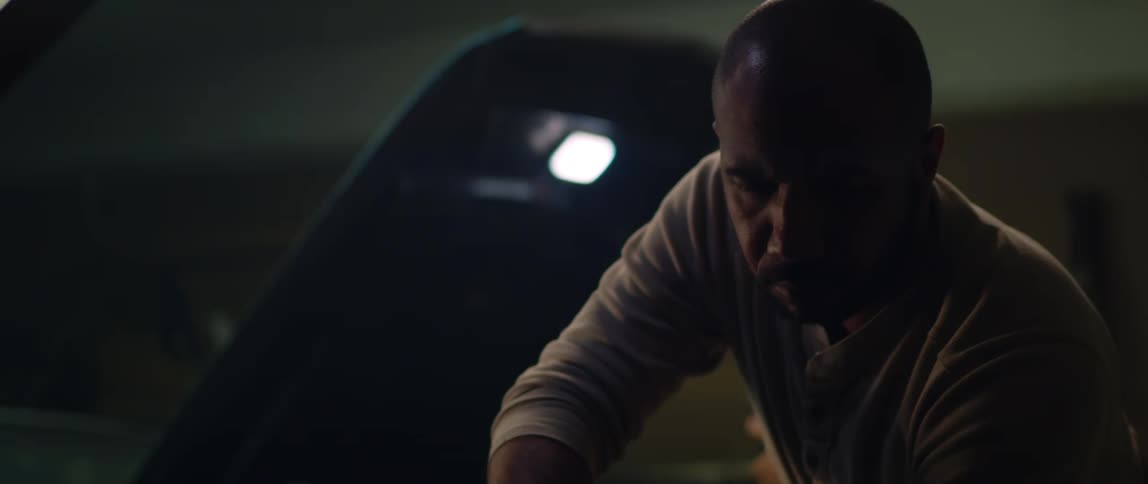 Mechanic uses a tool to repair the engine of a car inside a dimly lit garage