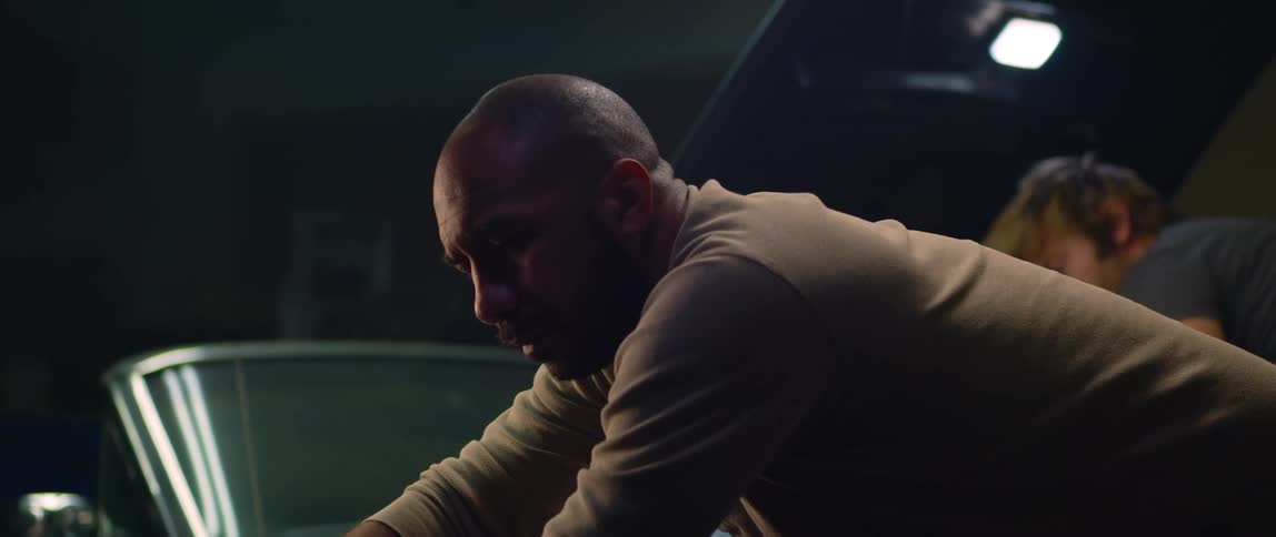 Two men work on the engines of two different cars parked in a garage