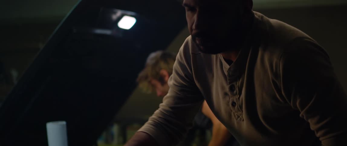 Mechanic looking at the engine of a car parked inside a dimly lit garage