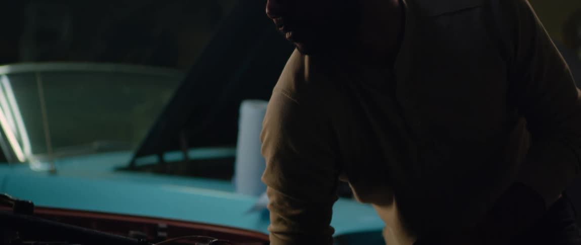 Mechanic looking at the engine of a car parked inside a dimly lit garage