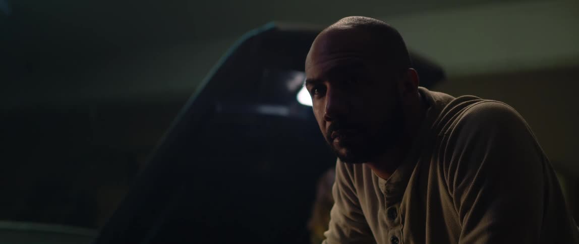 A man leans down as a mechanic looks under the hood of his car