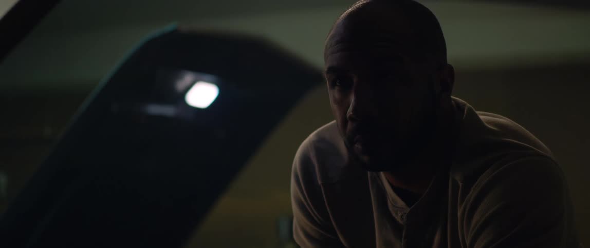 A man is working under the hood of a car and there is another man working on a car behind him