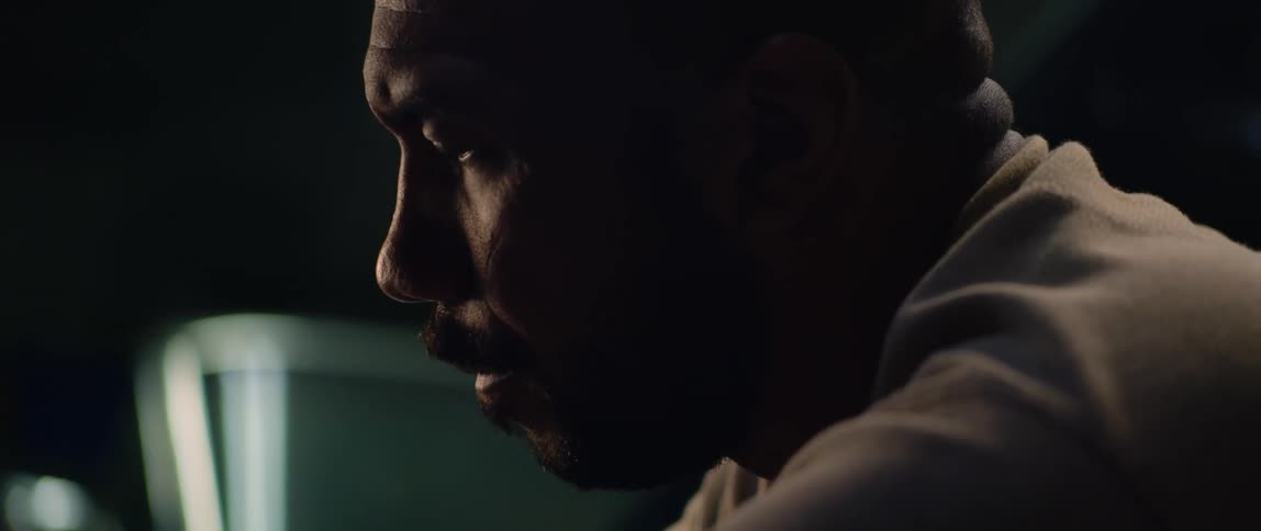 A man is in a dark room and he looks down as light shines on his face