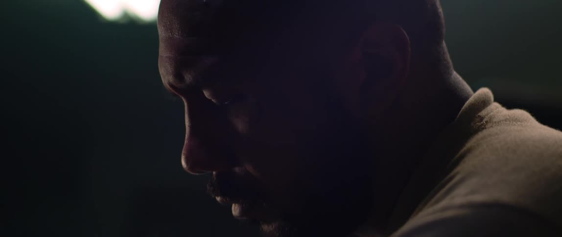 Close up of the face of a bald bearded man working inside a dimly lit garage