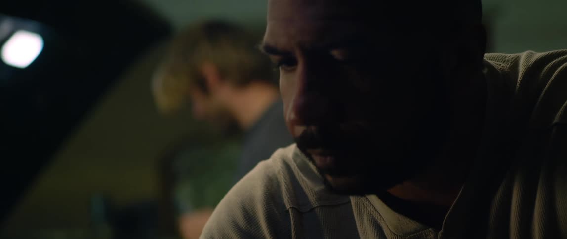 A mechanic looks under the hood of a car as a man looks around and then turns and looks at him