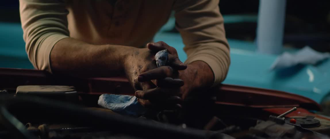 A man is holding a tool under the hood of a car with both hands clasped together