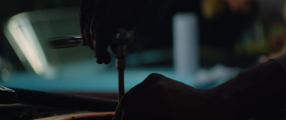 One person works on car engine as another mechanic leans over a second car