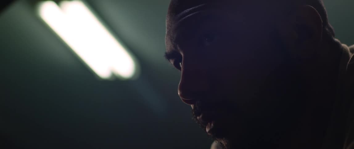 A man is in a dark room and he looks down as light shines on his face from above