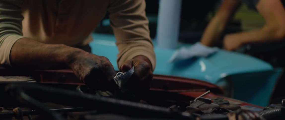 Bald male car mechanic with beard brown sweatshirt jeans and greasy hands repairs car engine at the garage