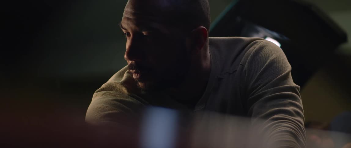 A man looking at a car thinking while a mechanic works behind him under a car hood