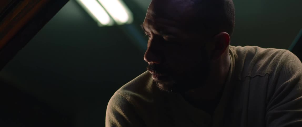 A man is in a dark room working under the hood of an automobile as light shines on his face from above