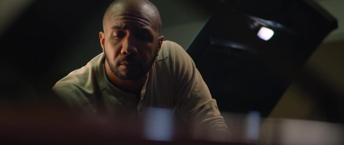 A man is looking around under the hood of a car as another man works on a car behind him