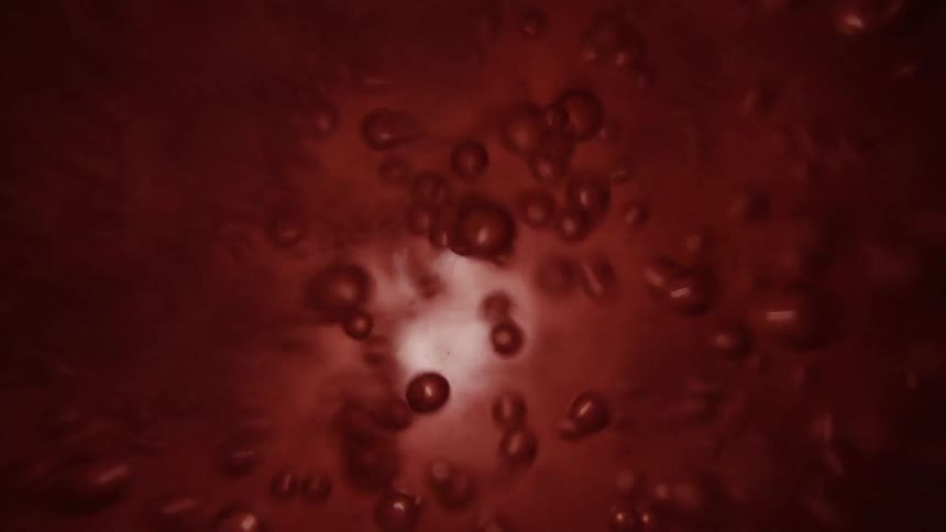 Light reflects on bubbles as they move rapidly in an orange liquid