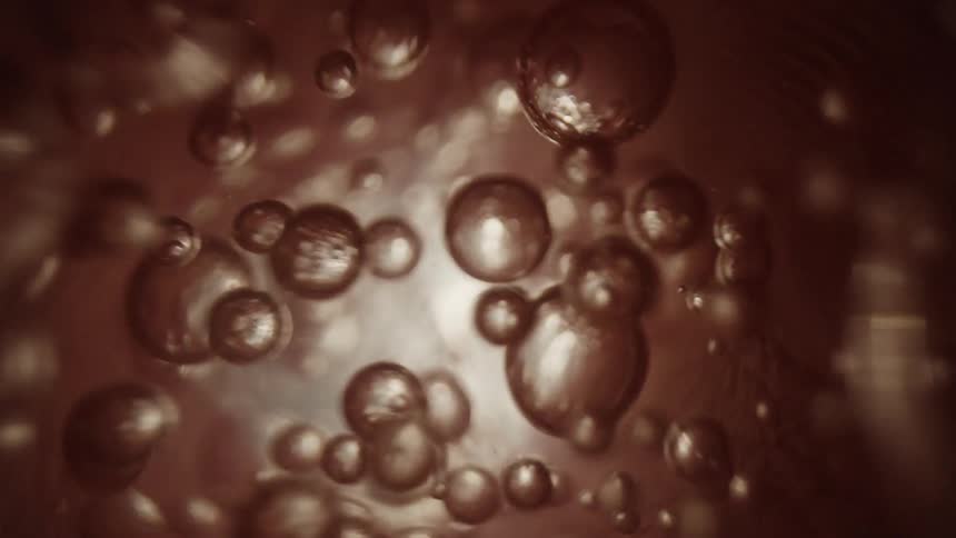 Bubbles rising up popping and splitting in a brown liquid with light glowing