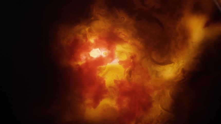 A bright orange organic cloud glows as it moves in the darkness