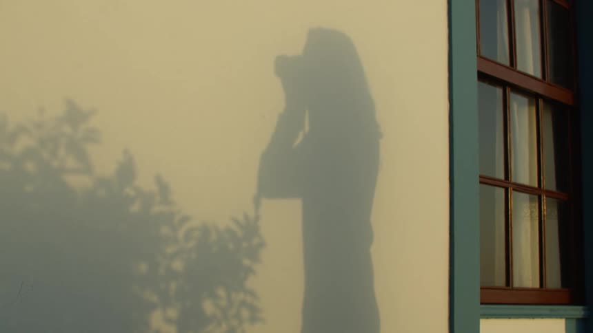 A shadow on a wall shows a woman using a camera to take a picture