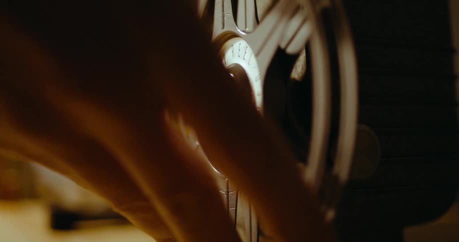 A hand places an empty reel onto a projector