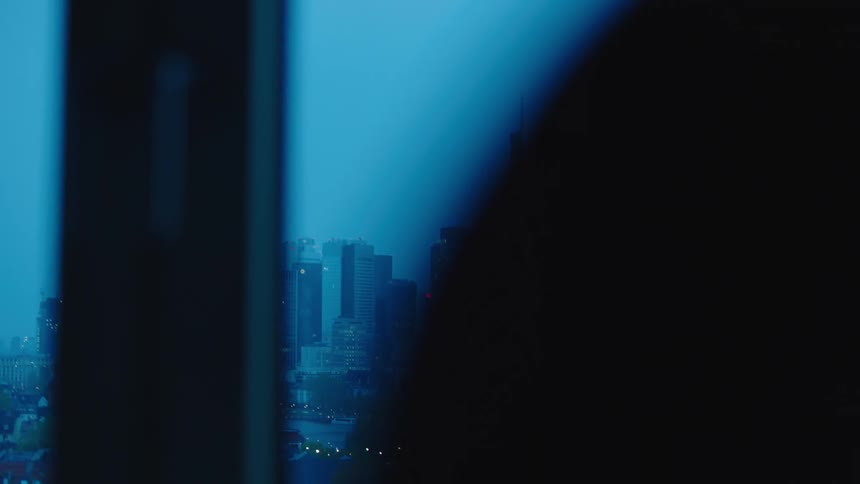 A person holds a mug while looking out their window to the city skyline