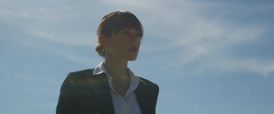 A woman stands outside while the sun shines down and looks off in to the distance