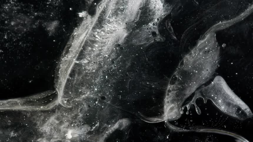 A gray liquid like substance moves among small bubbles in the darkness