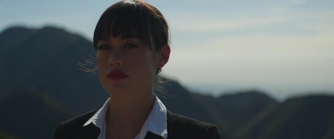 A woman stands in front of hills and looks off in to the distance