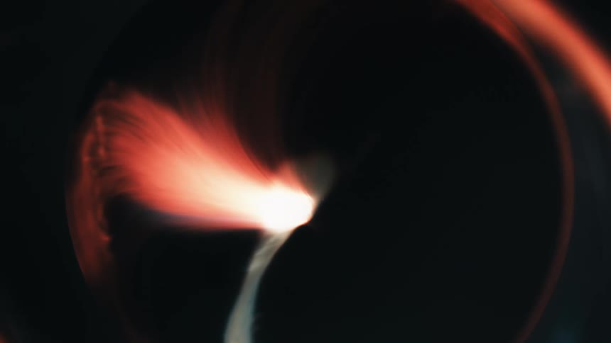 A circle of light expands against black with a flare of orange