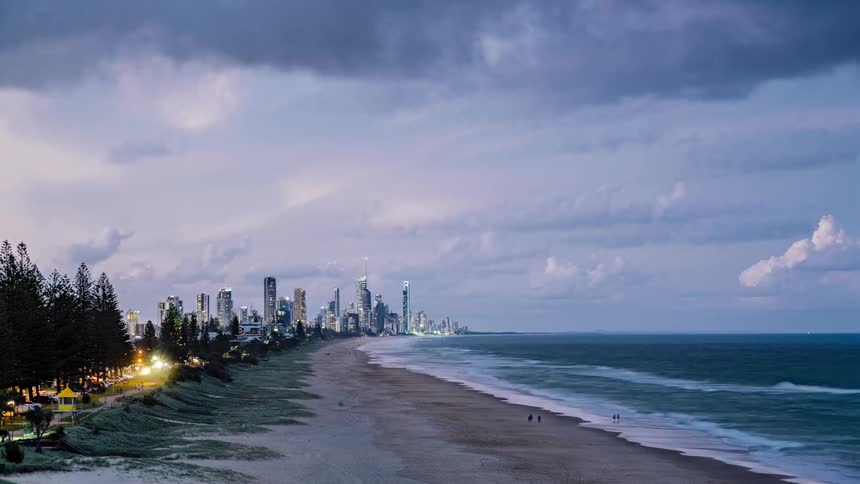 Clouds roll over the beach next to the city as people walk on the sand
