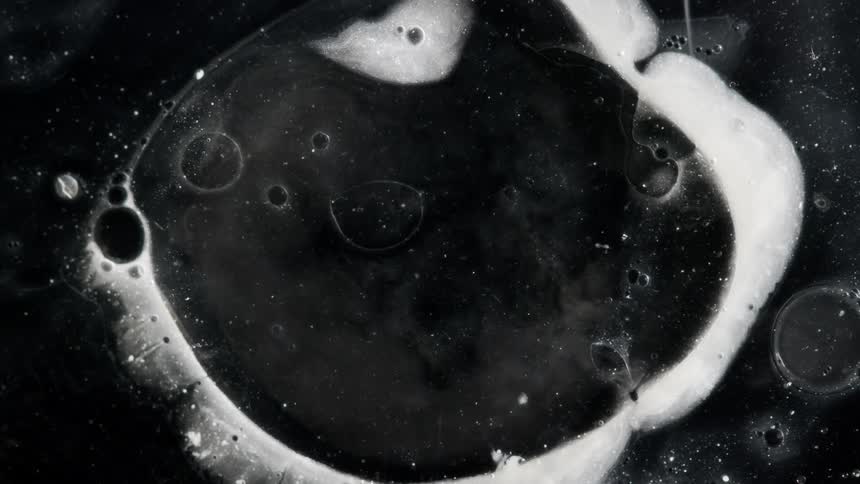 A circle of white wispy foam shifts and morphs against black