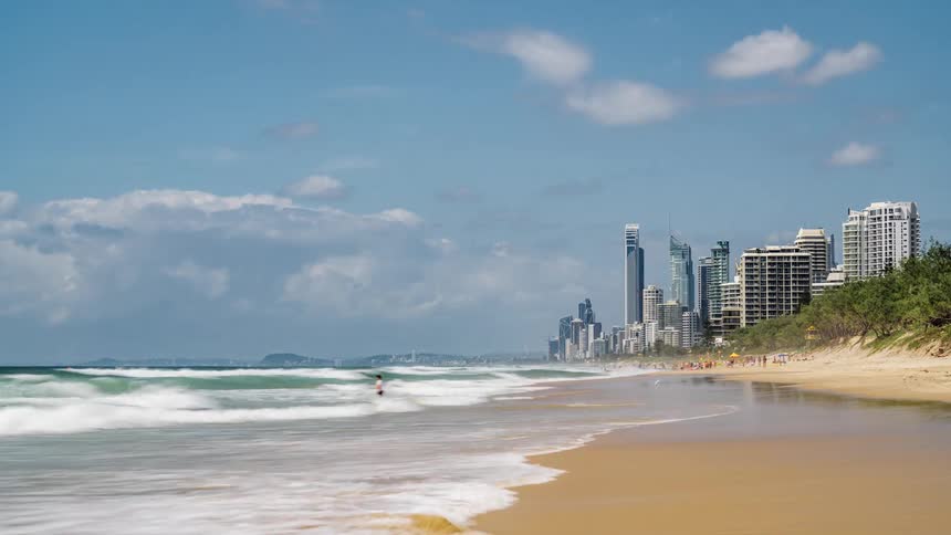 Waves wash into a beach on the coast of a metropolis during the day