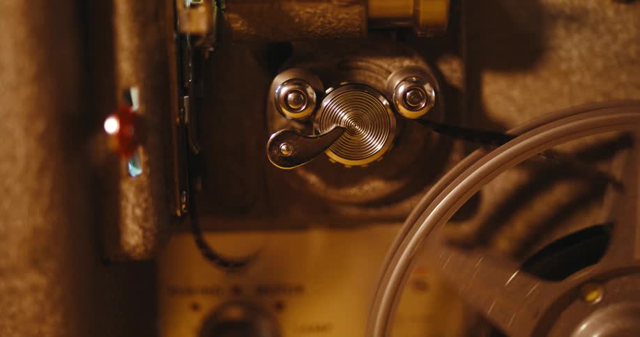 A person turns a knob on a vintage film projector as film spins through