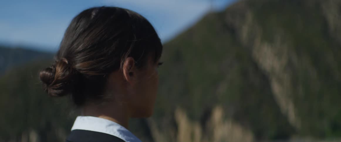 A woman is standing outside with her hair tied up behind her head as she is looking away